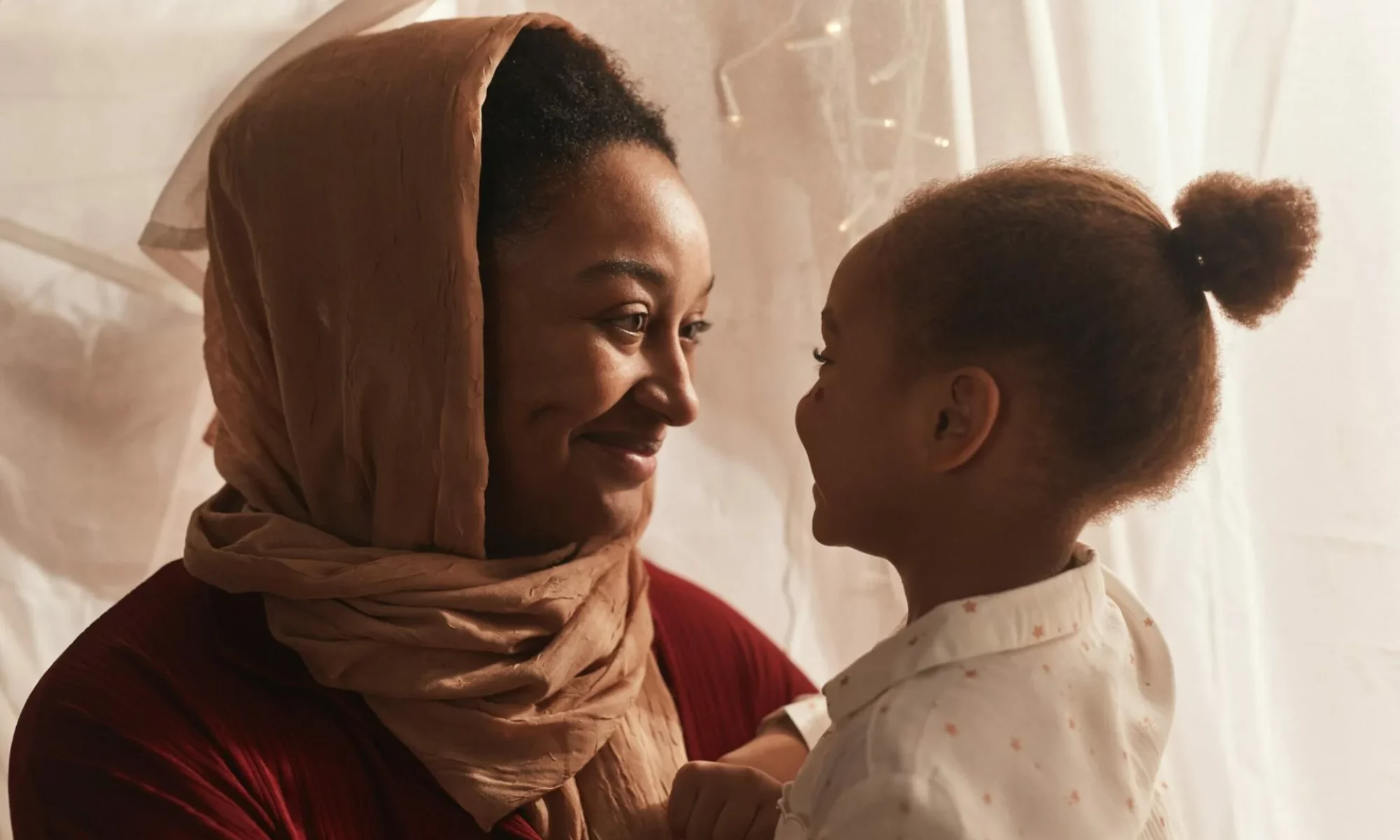 Smiling woman in a hijab looking lovingly at a young girl, symbolizing community, connection, and empowerment within families of African descent.